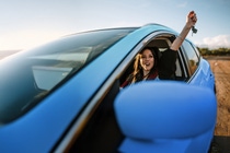 Woman in a blue car holding her arm up out of the window Woman in a blue car holding her arm up out of the window