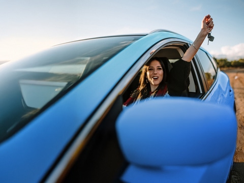 Woman in a blue car holding her arm up out of the window Woman in a blue car holding her arm up out of the window